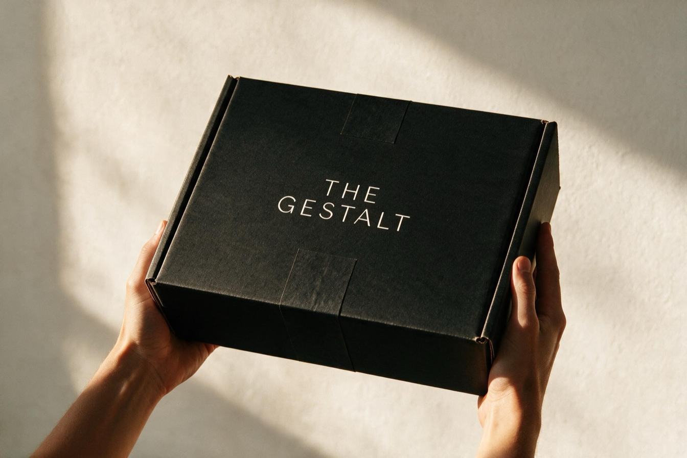 Руки протягивают закрытую чёрную коробку THE GESTALT