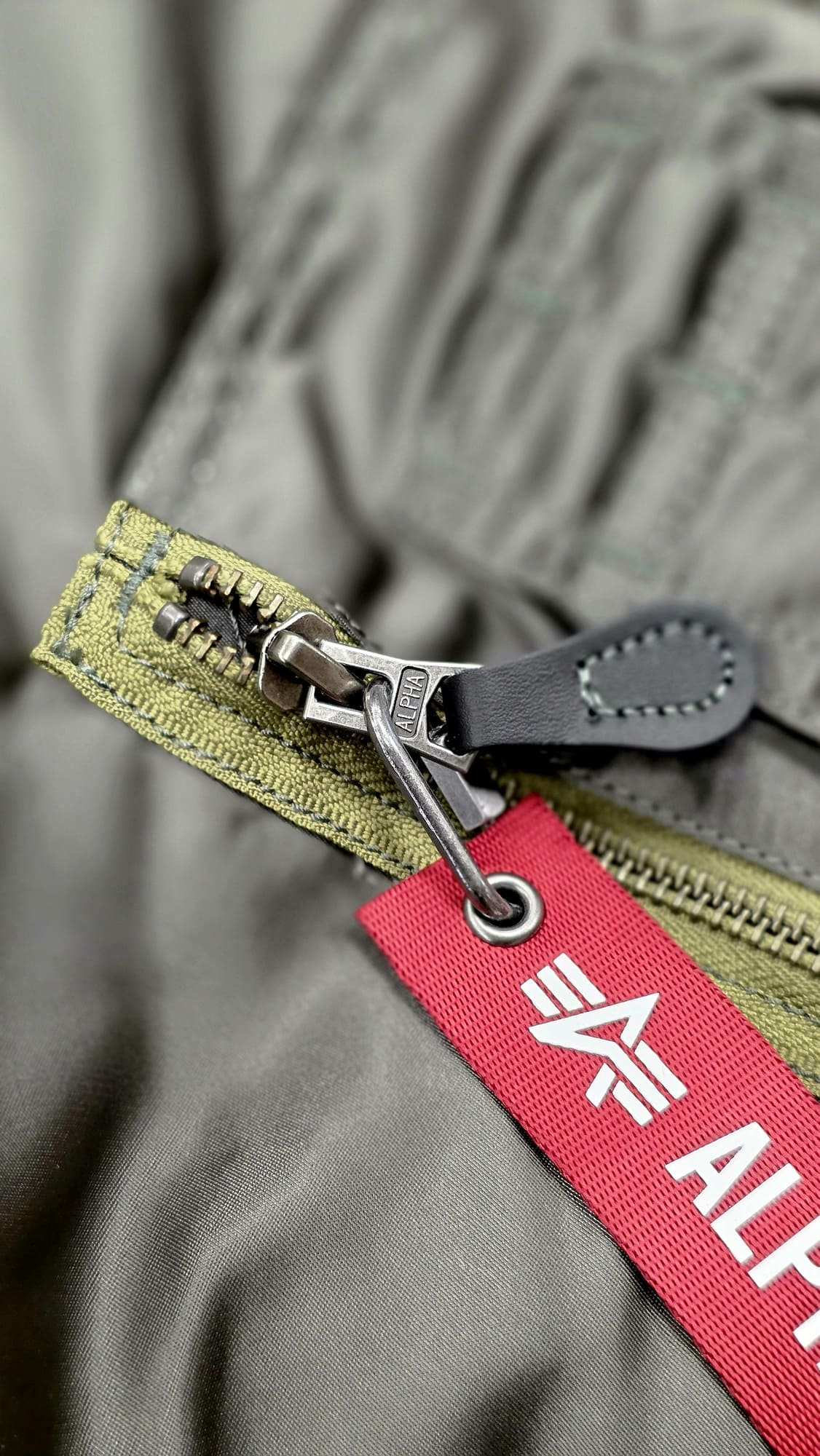 Бегунок с кожаным язычком и красной лентой на современной куртке Alpha Industries