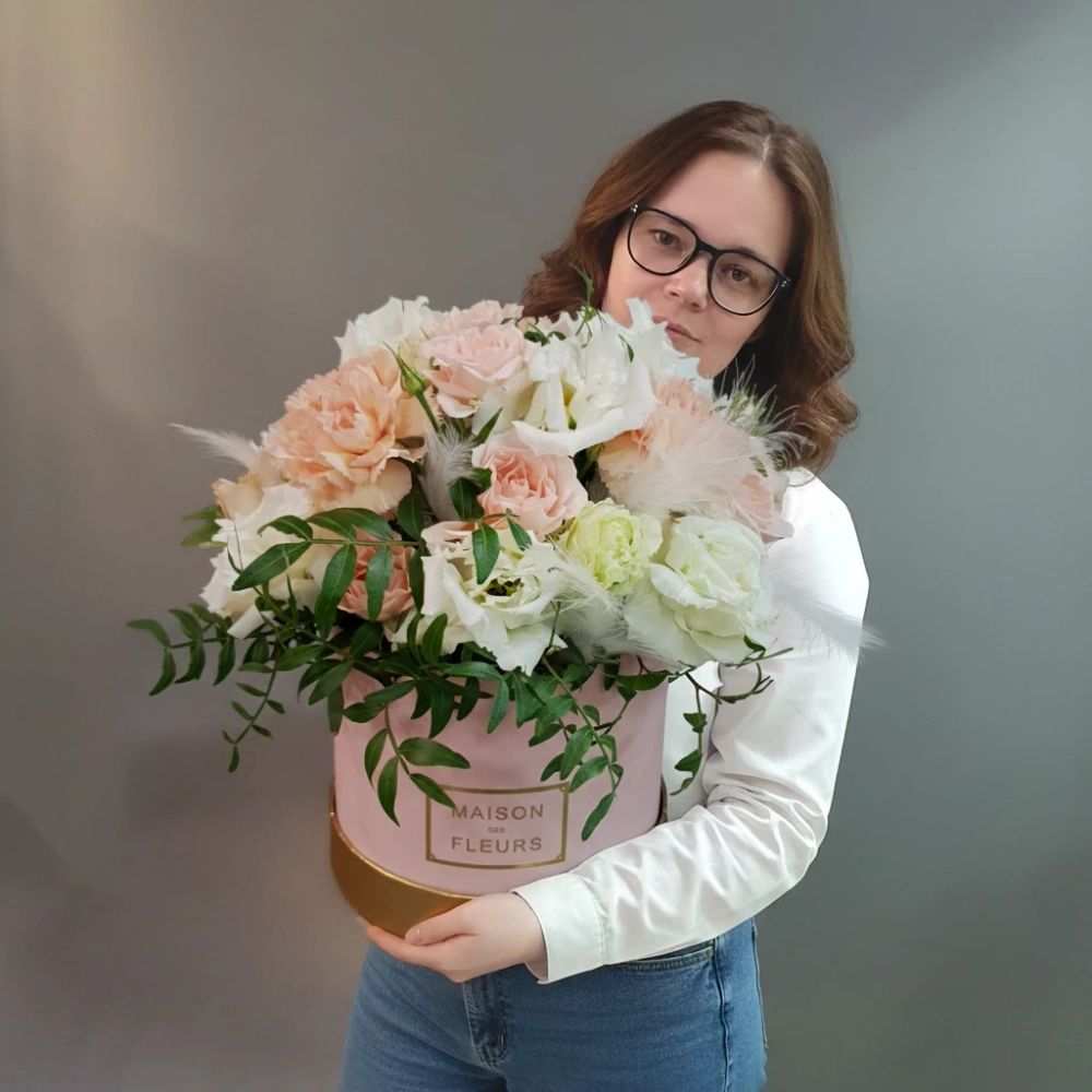 Белая махровая эустома, кремовая кустовая роза, нежно-розовый диантус, фисташка и белые перья в розовой шляпной коробке.