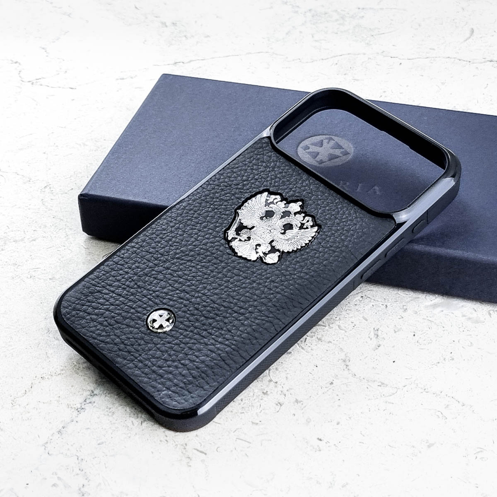 Чехол iPhone 18 Pro Max Euphoria HM Premium Leather Black Герб РФ опирается на закрытую тёмно-синюю фирменную коробку с серебряным логотипом Euphoria открытая крышка рядом — серебряный металлический Государственный герб Российской Федерации двуглавый орёл короны скипетр держава Георгий Победоносец ювелирный сплав чёрная зернистая кожа Италия круглый шильд Euphoria светлый мрамор студия