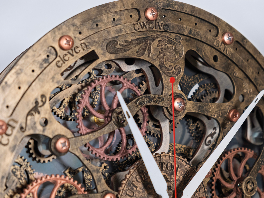 Крупный план механизма настенных часов Automaton Bite 1682 Старое Золото: открытый циферблат с медными и бронзовыми шестерёнками, белыми часовыми и минутными стрелками и красной секундной стрелкой — выразительный ретро‑декор в стиле стимпанк.