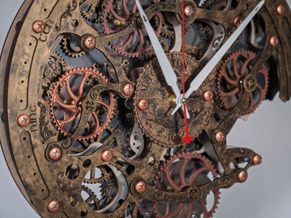 Крупный план настенных часов «Automaton Bite 1682»: сложный механизм из медных и бронзовых шестерёнок, красная секундная стрелка и белые часовая и минутная стрелки — ретро-стимпанк элемент для украшения дома или студии.