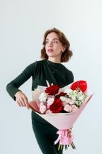 Девушка в тёмно-зелёном платье держит букет «Пламенный» с красными розами, розовыми кустовыми розами, белой маттиолой и красным антуриумом