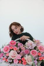 Крупный план женщины, держащей ручку белой корзины, наполненной розовыми и кремовыми цветами, герберами, розами и маттиолой